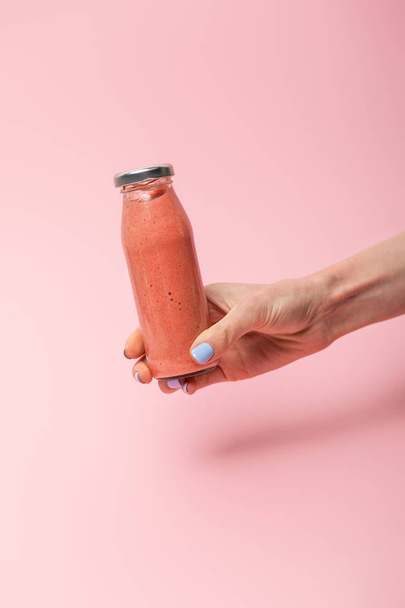 cropped view of woman holding glass bottle with tasty smoothie on pink  - 写真・画像