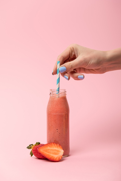 cropped view of woman holding straw in glass bottle with tasty smoothie near ripe strawberries on pink  - 写真・画像