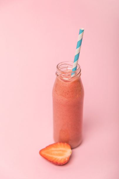 sweet and tasty smoothie in glass bottle with straw near ripe strawberries isolated on pink  - Foto, afbeelding