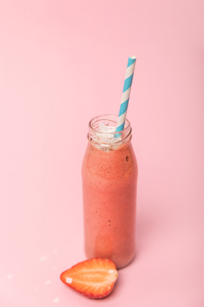 sweet and tasty smoothie in glass bottle with straw near red strawberry on pink  - Foto, afbeelding