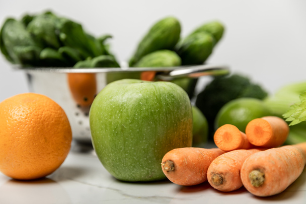selective focus of green apple, orange and carrots near green cucumbers on white  - Photo, Image