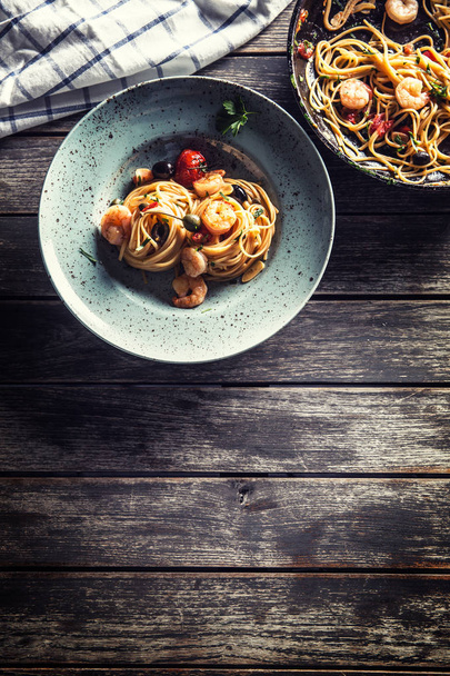 Pasta spaghetti on plate and pan with shrimp tomato sauce toatoes and herbs. Italian or mediterranean cuisine - 写真・画像
