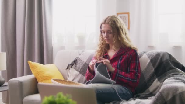 Zoom in of woman sitting on sofa and knitting crochet clothes in cozy home - Materiał filmowy, wideo