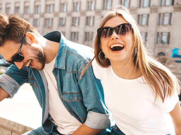 Portrait of smiling beautiful girl and her handsome boyfriend in casual summer clothes and sunglasses. Happy cheerful family having fun on the street background. Hugging - Zdjęcie, obraz