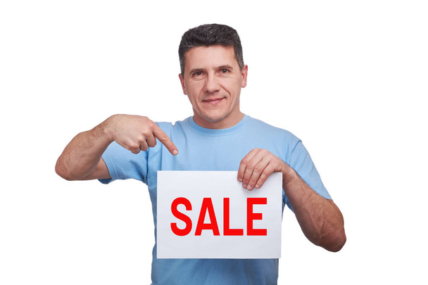 Handsome man with smiling face holding paper with word sale and making gesture pointing his finger at him from above - Foto, imagen