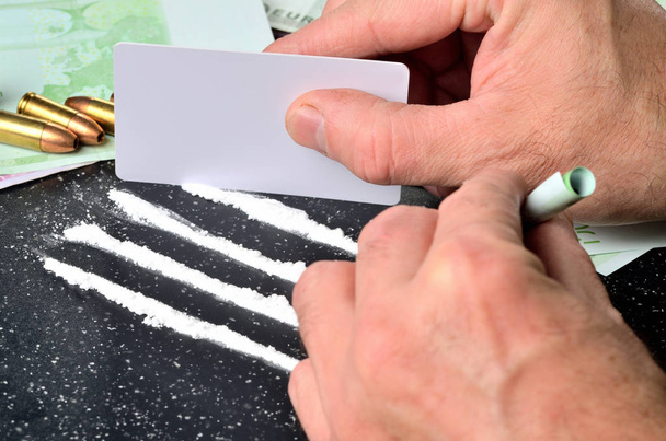 Człowiek co linii kokainy przy użyciu białej karty, pistolet amunicji w tle - Zdjęcie, obraz