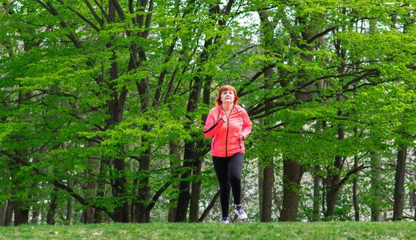 Mujer de mediana edad que usa ropa deportiva y corre en el bosque
 - Foto, Imagen