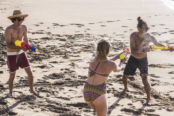 Youthful and people playing with water guns at beach during vacation  - Photo, Image