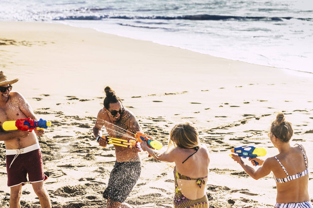 Jugendliche und Menschen, die im Urlaub am Strand mit Wasserpistolen spielen  - Foto, Bild