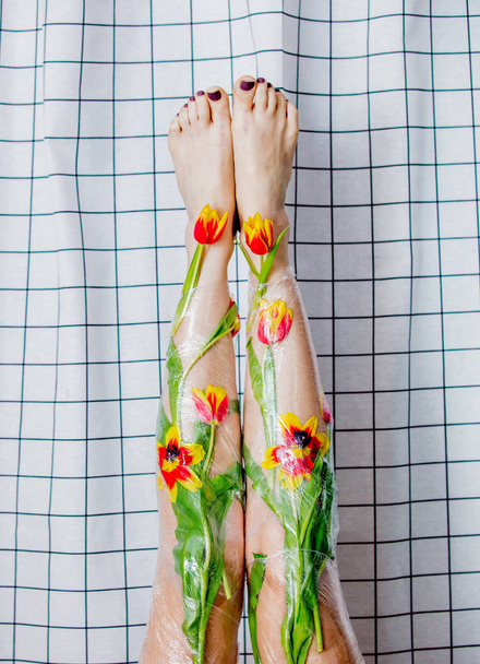 mujer sostiene sus piernas envueltas con celofán y flores
. - Foto, imagen