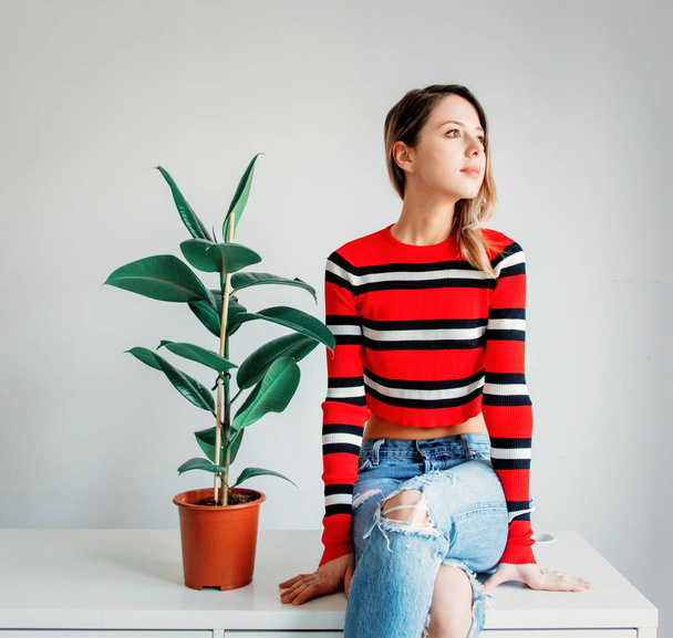 young woman in sptriped sweater and jeans sitting on a table nea - Фото, зображення