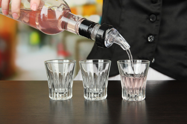 Barmen hand with bottle pouring beverage into glasses, on bright background - Photo, image