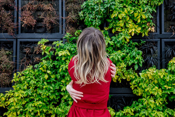 young girl hugging herself against a wall with plants - Photo, image