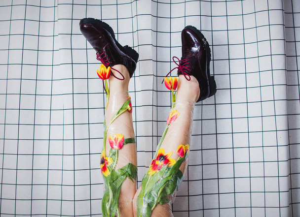 woman holds her legs up wrapped with cellophane and tulips flowe - Photo, Image