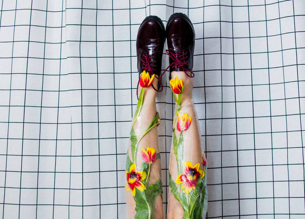 Женщина держит ноги завернутыми целлофаном и тюльпанами.
 - Фото, изображение