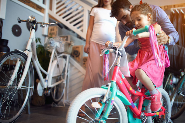 Young family buying new bicycle for little girl in bike shop - Foto, afbeelding