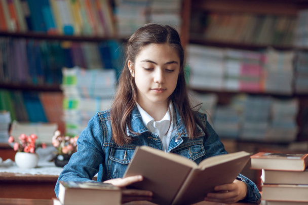 όμορφη μαθήτρια κάθεται στη βιβλιοθήκη και διαβάζοντας ένα βιβλίο - Φωτογραφία, εικόνα