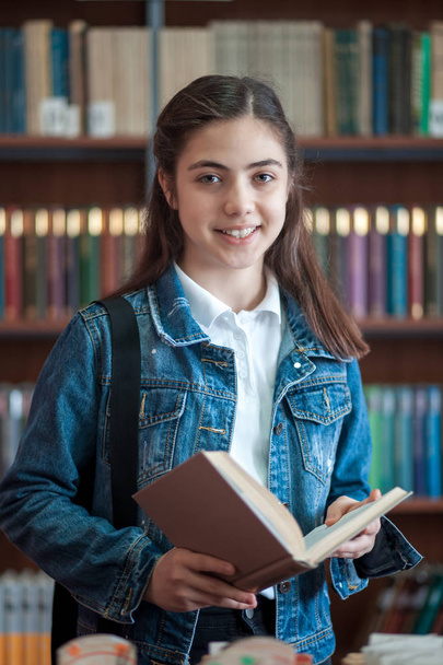 beautiful schoolgirl in the library reading a book - Foto, Imagem
