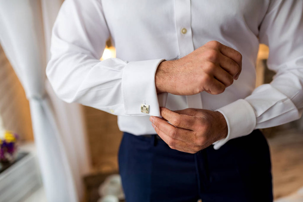 A groom putting on cufflinks as he gets dressed in formal wear. Man getting ready for work. - Фото, изображение