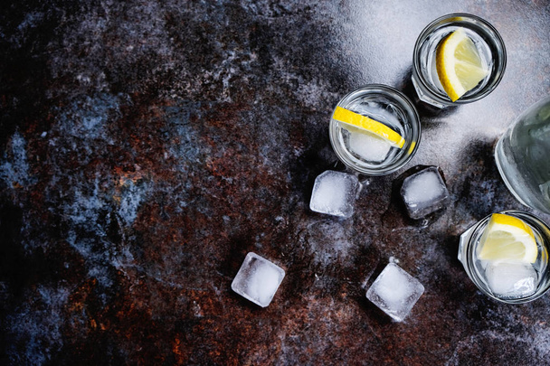 Koude wodka in shot glazen met citroen op stenen achtergrond. Bovenaanzicht, kopie ruimte. - Foto, afbeelding