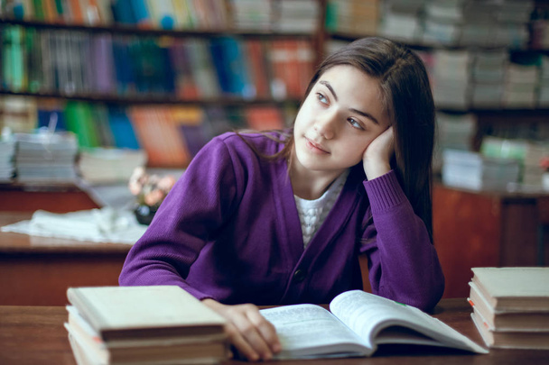 szép iskoláslány ül a könyvtárban, és egy könyvet olvasott - Fotó, kép