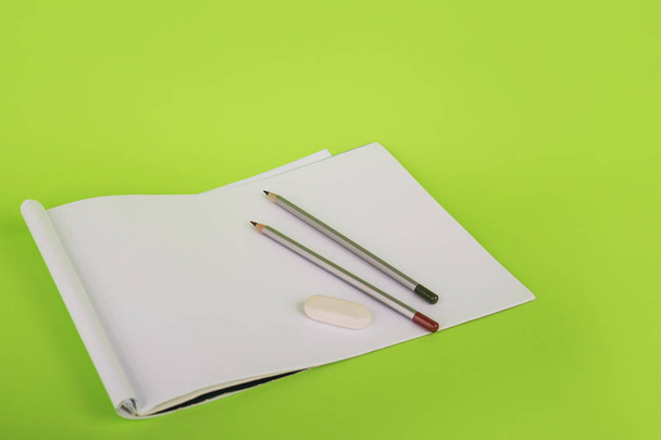 White paper and two pencils on a green background. Album for drawing and pencils. The artist draws. stationery on a green background - Foto, afbeelding
