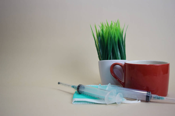 Close up protective face green mask, coffee cup and syringe isolated on brown background - Photo, Image