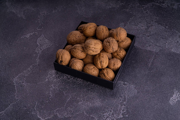 Whole and cracked walnuts on a square plate on blue textured surface, side view. Healthy nuts and seeds composition. - Foto, Imagem