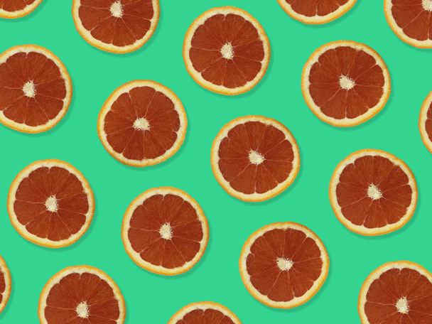Patrón creativo hecho de naranjas rojas. vista superior del patrón de fruta colorida de rodajas de naranja roja fresca sobre fondo verde colorido
.  - Foto, Imagen