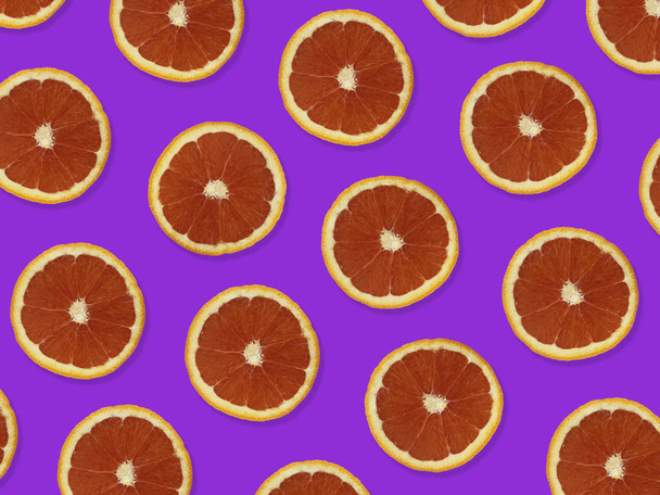 Δημιουργικό μοτίβο φτιαγμένο από κόκκινα πορτοκάλια. Κορυφαία θέα του πολύχρωμου φρούτου μοτίβο φρέσκων κόκκινων φέτες πορτοκαλιού σε μωβ πολύχρωμο φόντο.  - Φωτογραφία, εικόνα
