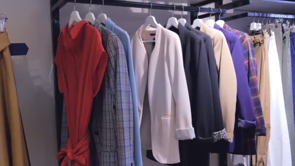 Γυρίσματα στολή γυναίκα κρεμάστρες συνεχώς στο κατάστημα σε εσωτερικούς χώρους. Κλείστε τα ρούχα shot στο σκορ, μεγάλη γραμμή με φορέματα, φούστες, παλτά, πουλόβερ, σακάκια, παντελόνια - Πλάνα, βίντεο