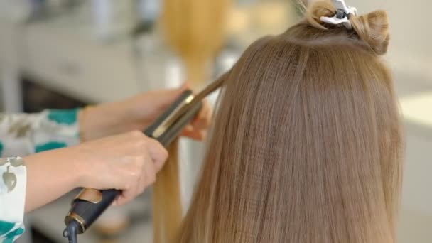 Egy nő fodrász csinál egy terjedelmes frizura, hogy az ügyfél segítségével a haj ironer, préseléséhez haj. Professzionális fodrász a munkahelyen. lassított mozgás - Felvétel, videó