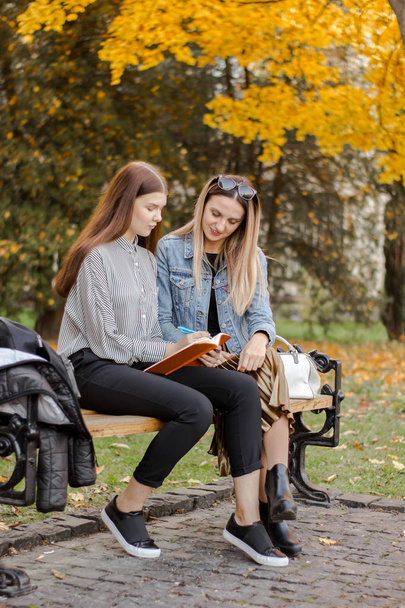 Kız arkadaşları sonbahar parkında bir bankta otururken notlar almak - Fotoğraf, Görsel