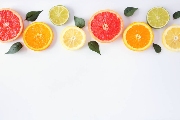 Colorful fruit border of fresh citrus slices with leaves. Top view, flat lay over a white background with copy space. - Zdjęcie, obraz