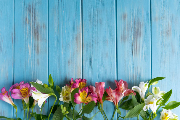 Blahopřání k narozeninám-šablona Modrý dřevěný podklad s růžovými květy alstroemerie. Základna pro blahogratulační prapor. Nápis s květinami a copispeymi. - Fotografie, Obrázek