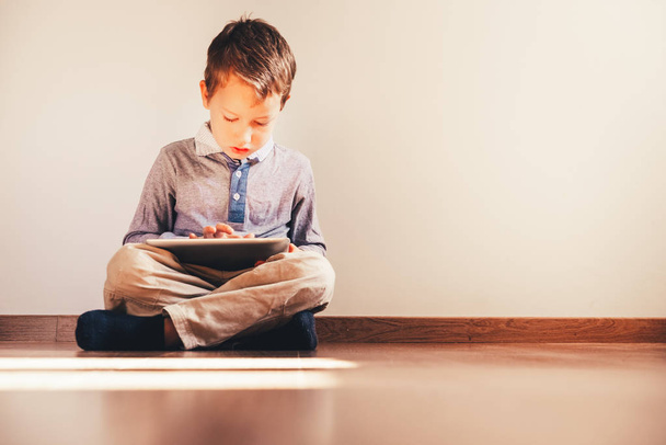Junge sitzt mit digitalem Tablet in der Hand auf dem Boden - Foto, Bild