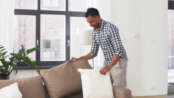 indian man arranging sofa cushions at home - Filmati, video