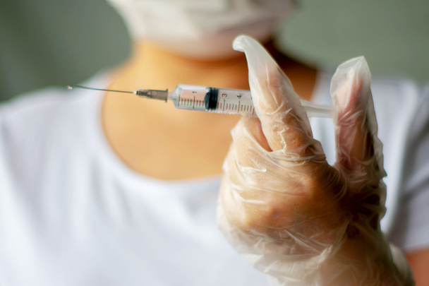 Hands of a physician wearing protective white gloves prepare a syringe shot closeup. - Foto, afbeelding