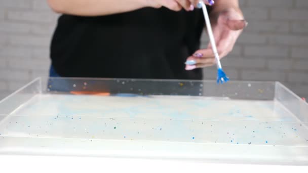 Samička Ebru umělkyně s kartáčem v ruce. V pohybu je abstraktní barva. Psychedelický záběr na pozadí. Barevná místa. Ebru umění. Zavři to. Barevná hladina vody. Vystříknutí modré barvy mramoru - Záběry, video