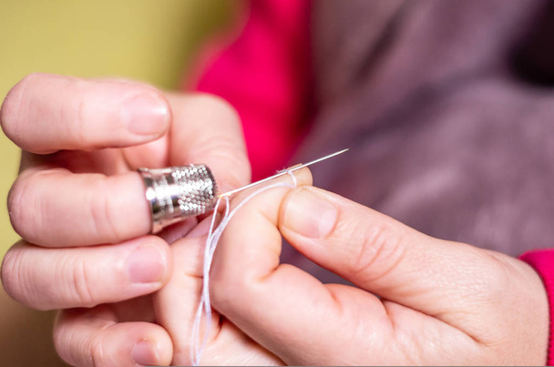 eine Hand mit Fingerhut-Knoten und das Abschneiden eines Fadens auf einer Nadel in einer Nähstunde - Foto, Bild