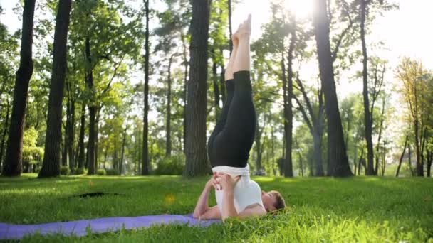 4k Zeitlupenvideo von Yoga und Fitness auf Gras im Park. Lächelnde Frau mittleren Alters, die an einem sonnigen Tag im Wald praktiziert und Übungen macht. Frau kümmert sich um ihre geistige und körperliche Gesundheit - Filmmaterial, Video