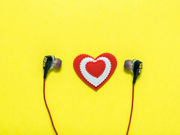 Heart of white and red colors in earphones on yellow background. Flat lay. - Photo, Image