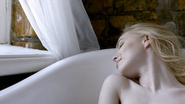 Kaunis tyttö seksikäs blondi aamulla poseeraa kylpyhuoneessa. Toimintaa. Nuori blondi nainen makaa kylvyssä aamulla
 - Valokuva, kuva