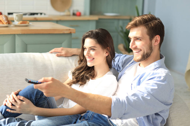 Young loving couple on sofa at home watching tv and laughing. - Photo, Image
