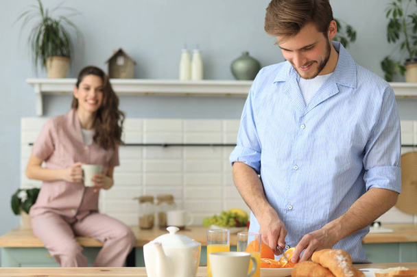 Portrait of happy young couple in pajamas cooking together in the kitchen, drinking orange juice in the morning at home. - Photo, image