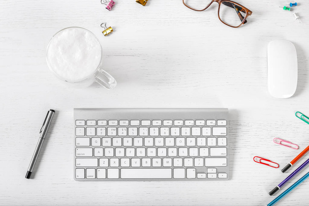 Biurko biurowe na białym tle drewna. Przestrzeń robocza z klawiaturą, myszą, ołówkiem, okularami, notebookiem i filiżanką latte. Płaski lay - Zdjęcie, obraz
