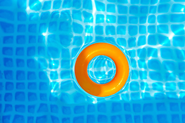 Апельсиновое надувное кольцо плавающее в бассейне в солнечный день, вид сверху
 - Фото, изображение