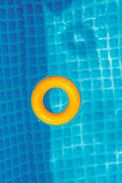 κίτρινο φουσκωτό δαχτυλίδι που επιπλέει στην πισίνα την ηλιόλουστη μέρα, κορυφή θέα - Φωτογραφία, εικόνα