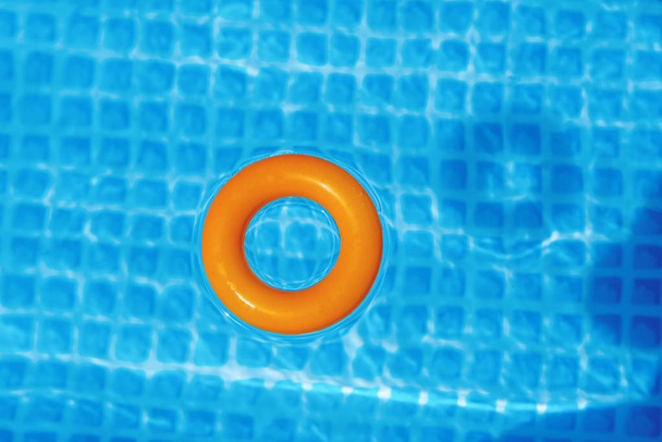 Oranje opblaasbare ring drijvend in zwembad op een zonnige dag, bovenaanzicht - Foto, afbeelding