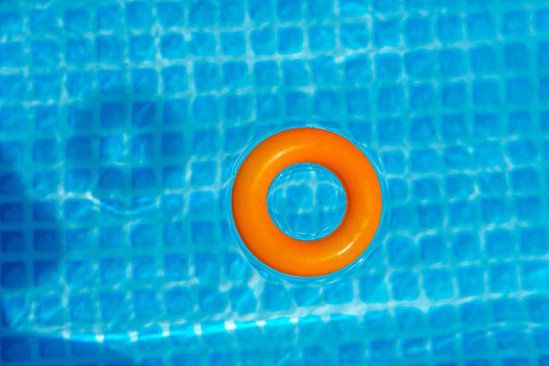 anel inflável de laranja flutuando na piscina no dia ensolarado, vista superior
 - Foto, Imagem